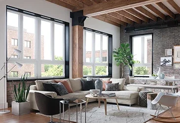 Modern Loft apartment living room featuring several tall windows. The room has exposed rafter ceilings, a brick wall and a large l shaped sectional.